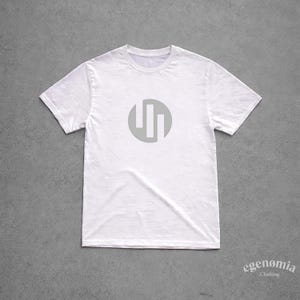 May include: White crew neck t-shirt with a gray circular logo featuring three vertical lines. The shirt is made of a soft material and is displayed on a gray background. The brand name "egenomia clothing" is printed in a script font.