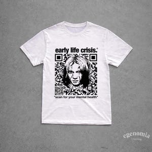 May include: White t-shirt with a black and white graphic. The graphic features a QR code design with a portrait and the text "early life crisis." Below the image is the text "scan for your mental health."