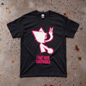 May include: A black short-sleeve t-shirt featuring a stylized hot pink graphic of a creature with pointed ears holding a small square object. Below the graphic, the text reads I DONT KNOW CONSEQUENCE in bold hot pink capital letters.