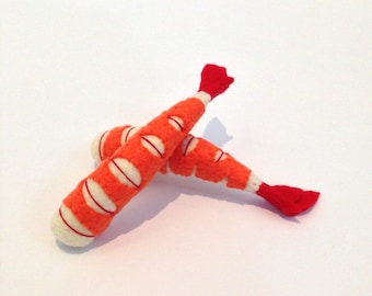 May include: Two felt shrimp toys, one orange and white with a red tail, the other orange and white with a red tail, lying on a white surface.