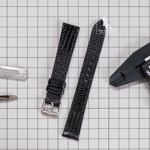 May include: A black textured watch strap with a silver-toned metal buckle, positioned on a white grid background alongside a metal tool and a black digital caliper. The logo Luu Leather is visible in the upper right corner of the image.