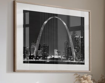 May include: A light beige sectional sofa with multiple pillows in a living room setting. The sofa is positioned in front of a large window with a view of trees. A black and white photograph of the St. Louis Arch is hanging on the wall.
