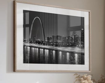 May include: A beige sectional sofa with multiple pillows in a living room with a large window, a wooden coffee table, and a black and white photograph of the St. Louis Arch.
