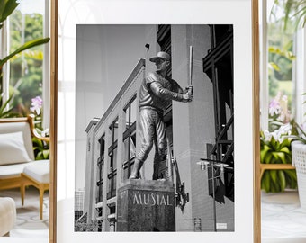 May include: Black and white photograph of a bronze statue of a baseball player holding a bat. The statue is standing in front of a building with the name "Musial" on the base.