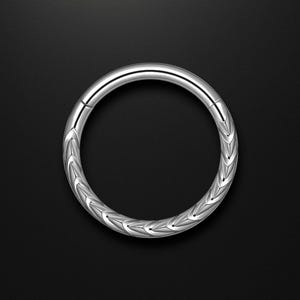 Könnte beinhalten: Ein silberfarbener, kreisförmiger Körperschmuck mit einem strukturierten, sich wiederholenden Muster. Das Schmuckstück ist ein nahtloser Ring, der zum Tragen in einem Piercing bestimmt ist. Der Hintergrund ist einfarbig schwarz.