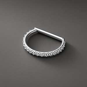 May include: A silver-toned D-shaped hoop ring featuring a straight bar segment and a curved section adorned with a continuous row of small, clear, round-cut stones set along the outer edge, creating a polished and reflective metallic appearance.