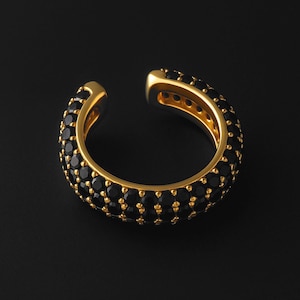 May include: A gold ear cuff adorned with black gemstones. The cuff curves around the ear, with a smooth, polished gold interior. The black stones are evenly spaced, creating a sparkling effect against the gold.