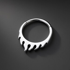 May include: A polished silver-tone circular hoop ring featuring a decorative flame-like design along the bottom half. The jewelry piece has a smooth, reflective metallic finish and a hinged segment closure mechanism visible at the top of the hoop.
