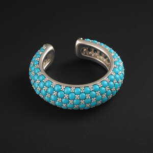 May include: A silver ear cuff with a turquoise bead design. The cuff is open at one end and features small, sparkling accents between the turquoise beads. The jewellery is set against a black background.