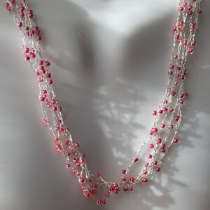 May include: A delicate silver necklace with multiple strands and small pink beads. The necklace is layered and has a cascading effect.
