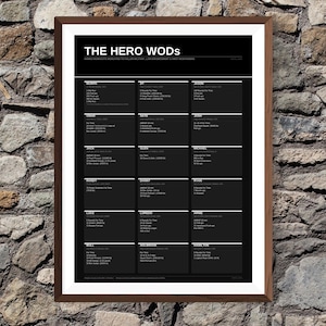 Könnte beinhalten: Ein gerahmter Schwarz-Weiß-Druck mit dem Titel "THE HERO WODS" mit Trainingsdetails, die gefallenen Militärangehörigen, Strafverfolgungsbeamten und Ersthelfern gewidmet sind. Der Druck befindet sich in einem braunen Rahmen und wird vor einer Steinmauer gezeigt.