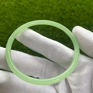 Könnte beinhalten: Ein hellgrünes Jade-Armband. Das Armband ist glatt und poliert.
