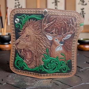 May include: A brown leather wallet with an embossed design of a roaring lion and a deer. The design includes green foliage and a black border. The wallet has a metal ring for attachment.