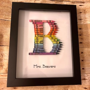 May include: A framed artwork featuring the letter "B" made from colorful crayons. The frame is black and the background is white. The text "Mrs. Beavers" is written below the letter.