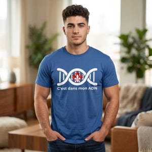 May include: A blue short-sleeved t-shirt featuring a white graphic of a DNA double helix strand with a red and white Canadian maple leaf emblem in the center. Below the graphic, the text reads C'est dans mon ADN in white lettering.