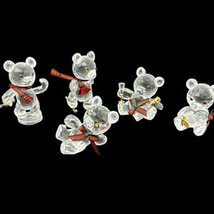 May include: Five crystal teddy bear figurines with red and green accents. The bears are wearing scarves and holding various objects.
