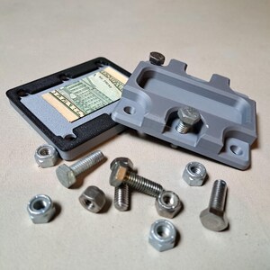 May include: A gray and black money holder with a hidden compartment, open to reveal a US dollar bill. The holder is accompanied by several silver bolts and nuts, suggesting a mechanical or industrial theme.