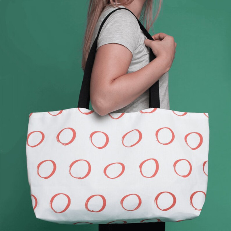 May include: A white tote bag with a repeating pattern of coral red circles. The bag has black straps.