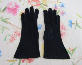 Pode incluir: Um par de luvas elegantes em azul marinho escuro. As luvas são longas, estendendo-se além do pulso, e apresentam uma borda ondulada. O tecido parece ser um material liso e fino. As luvas são exibidas em um fundo floral.