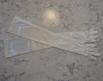 May include: A pair of long white satin gloves. The gloves are folded in half and the fingertips are visible.