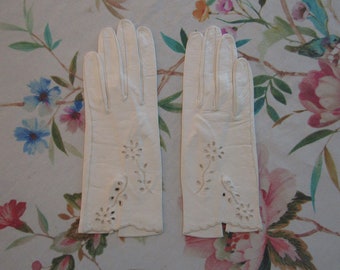 Puede incluir: Un par de guantes de cuero blanco con delicados recortes florales. Los guantes son largos y tienen un borde festoneado.