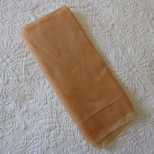 May include: A folded piece of sheer, light tan fabric with a fine, translucent mesh texture. The material is lightweight and semi-transparent, showing a consistent warm beige tone throughout the rectangular shape of the textile piece.