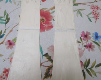 May include: A pair of long white leather gloves. The gloves are laying flat on a floral fabric background.