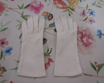 May include: Two white gloves, possibly for formal wear, are shown. They are made of a smooth fabric and have a traditional design with individual finger sections. The background is a floral pattern, with pink and blue flowers.