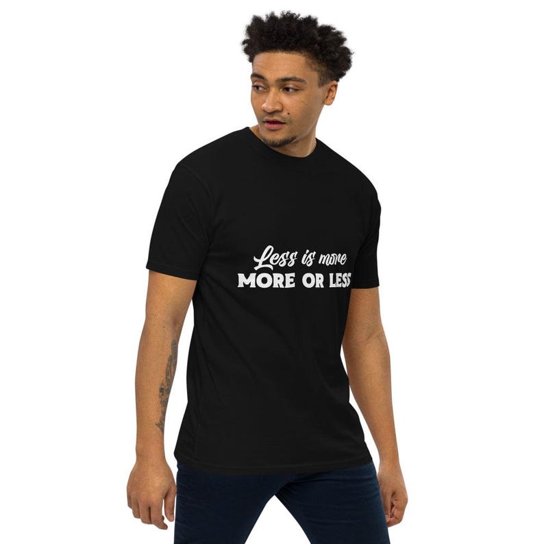 K&ouml;nnte beinhalten: Schwarzes T-Shirt mit dem wei&szlig;en Text "Less is more" &uuml;ber "MORE OR LESS". Das T-Shirt hat einen Rundhalsausschnitt und wird von einer Person getragen.
