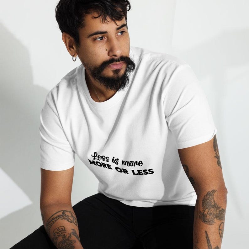 K&ouml;nnte beinhalten: Wei&szlig;es T-Shirt mit dem Text "Less is more MORE OR LESS" in schwarzer Schrift. Das T-Shirt hat einen Rundhalsausschnitt. Das Bild zeigt eine Person, die das T-Shirt tr&auml;gt.