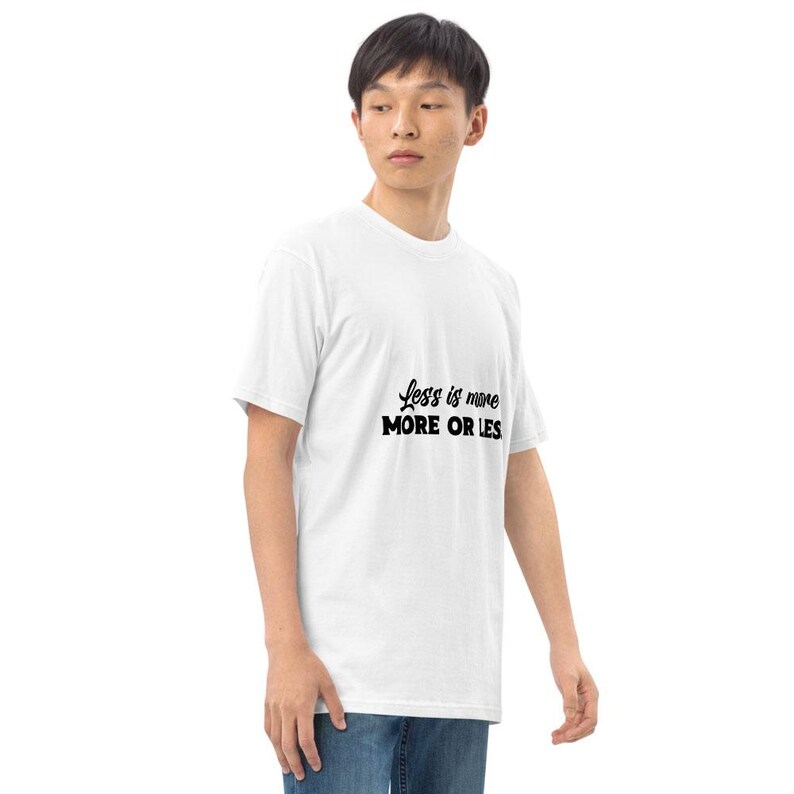 K&ouml;nnte beinhalten: Ein wei&szlig;es T-Shirt mit dem Text "Less is more MORE OR LES" in Schwarz. Das Shirt hat kurze &Auml;rmel und scheint aus einem weichen Material zu sein. Die Person tr&auml;gt eine blaue Jeans.
