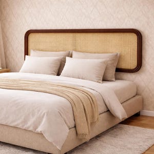May include: A bed with a woven rattan headboard and beige bedding. The headboard has a dark brown wooden frame. Beige pillows and a tan throw blanket are on the bed. The bed frame is upholstered in a light beige fabric.