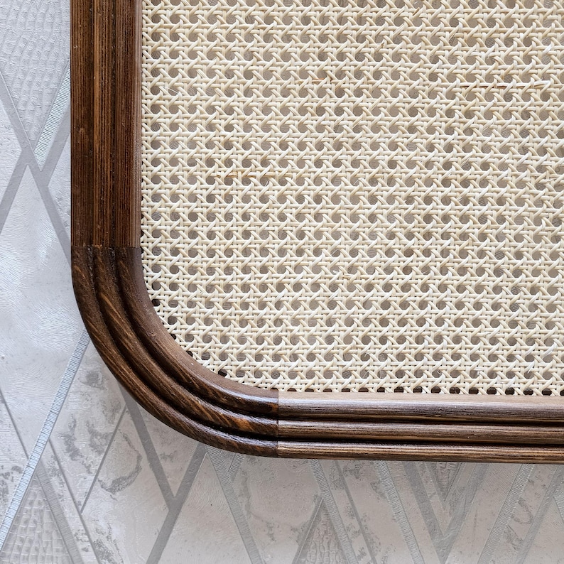 May include: Close-up of a section of a woven cane panel with a dark brown wooden frame. The cane has a light beige color and a detailed woven pattern. The frame has rounded corners and a smooth finish.