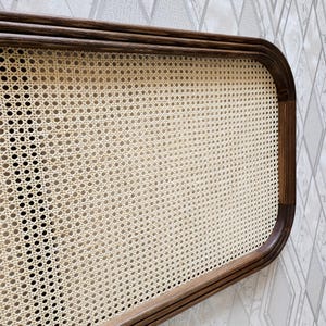 May include: A rectangular headboard with a woven cane center and a dark brown wooden frame. The headboard has rounded corners and a light beige woven pattern. The wooden frame has a smooth, polished finish.