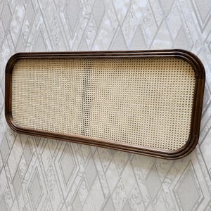 May include: Rectangular wooden frame with a woven cane insert. The frame has rounded corners and a dark brown finish. The cane insert is a light beige color and has a grid-like pattern.