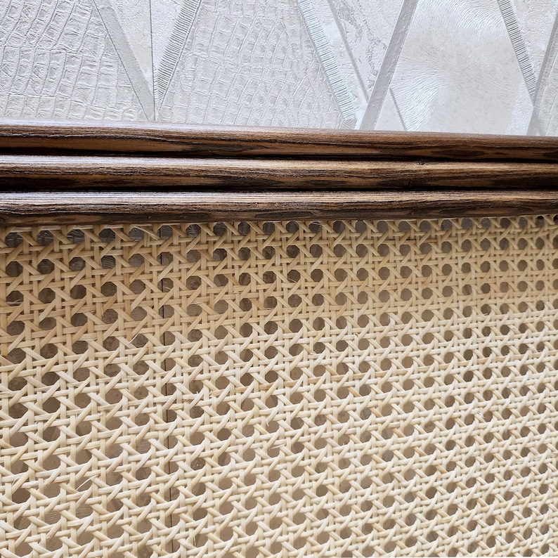 May include: Close-up of a section of a light-colored woven cane panel with a dark brown wooden frame. The cane has a repeating pattern of small, evenly spaced holes. The wooden frame has a smooth, polished finish.
