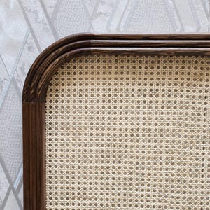 May include: Close-up of a section of a woven cane chair back. The frame is dark brown, with a curved top and a rectangular shape. The woven cane is a light beige color, creating a contrasting texture.