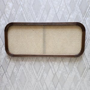 May include: Rectangular woven rattan tray with a dark brown wooden frame. The tray features a light beige woven center and rounded corners. The frame is a rich, dark brown color. The tray is designed for decorative or functional use.