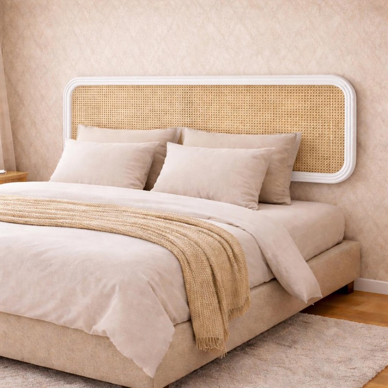 May include: A beige bed with a woven headboard and matching bedding. The headboard has a white frame and a woven cane insert. Beige pillows and a blanket are arranged on the bed, creating a cozy and inviting atmosphere.