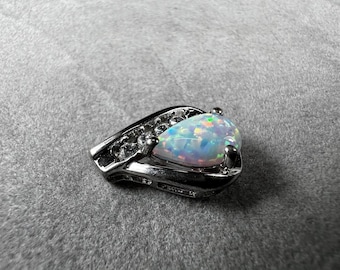 May include: A silver pendant featuring a pear-shaped opal gemstone. The opal displays a play of color with iridescent flashes of blue, green, and orange. The pendant has a decorative, openwork design on the sides.