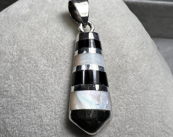 May include: A silver pendant with a geometric design. The pendant features alternating bands of black, white, and silver. The bottom of the pendant is a black, pointed shape. The top has a silver loop for a chain.