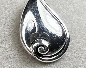 May include: A polished silver-toned teardrop-shaped brooch. The brooch features a swirling, scroll-like design at the base. The surface reflects light, creating highlights and shadows. The brooch is a jewelry item.