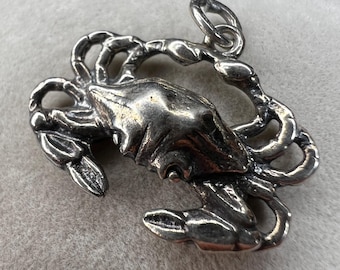 May include: A detailed silver crab pendant. The crab is depicted with intricate detailing, including claws, legs, and a textured shell. The pendant has a loop for attaching to a chain or necklace. The crab is a symbol of the Cancer zodiac sign.