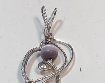 May include: A silver-toned pendant with a swirling design, featuring a lavender-colored bead at its center. The pendant's metalwork includes twisted and smooth sections, creating a unique, artistic look. The bail is a simple loop for a chain.