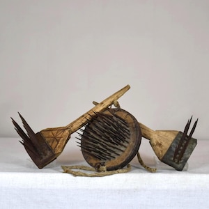 Può includere: Una collezione di tre antichi utensili in legno. Due utensili hanno un manico in legno con punte metalliche. Il terzo utensile è un oggetto rotondo in legno con punte metalliche. Gli utensili sono disposti su una superficie bianca.