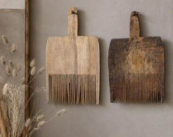Könnte beinhalten: Zwei antike Wollkämme aus Holz mit langen, dünnen, vertikalen Zinken und einem zentralen Griff. Ein Kamm ist aus hellem Holz, der andere aus dunklerem, verwittertem Holz. Beide haben ein kleines Loch oben am Griff zur Wandmontage.