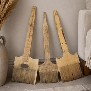 Puede incluir: Tres peines de lino antiguos de madera con mangos largos y dientes metálicos finos. Cada herramienta presenta una veta de madera marrón claro desgastada, una base rectangular plana y una fila densa de púas metálicas verticales finas.