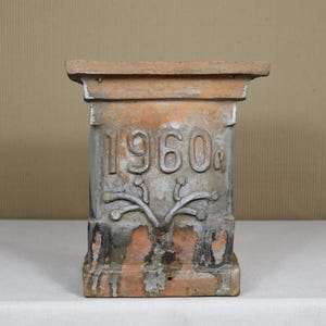 Puede incluir: Un pedestal de terracota con un acabado desgastado y el año "1960s" inscrito en la parte delantera.