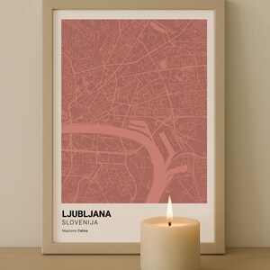 May include: A framed map print of Ljubljana, Slovenia, in a muted red hue, with the text "DIGITAL download" in the upper left corner. A lit candle sits in front of the map. The map is in a light-colored frame.