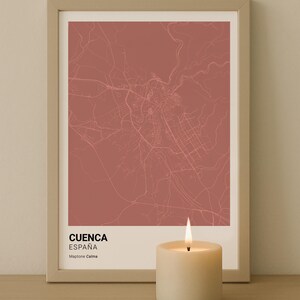 May include: Framed map print of Cuenca, Spain, in a muted red hue. The map is detailed with city streets and is labeled with the city name and country. A lit candle sits in front of the framed print.